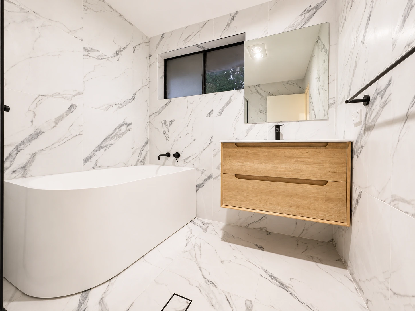 Castle Hill bathroom — freestanding bath and timber wall-hung vanity in full marble-look tiling