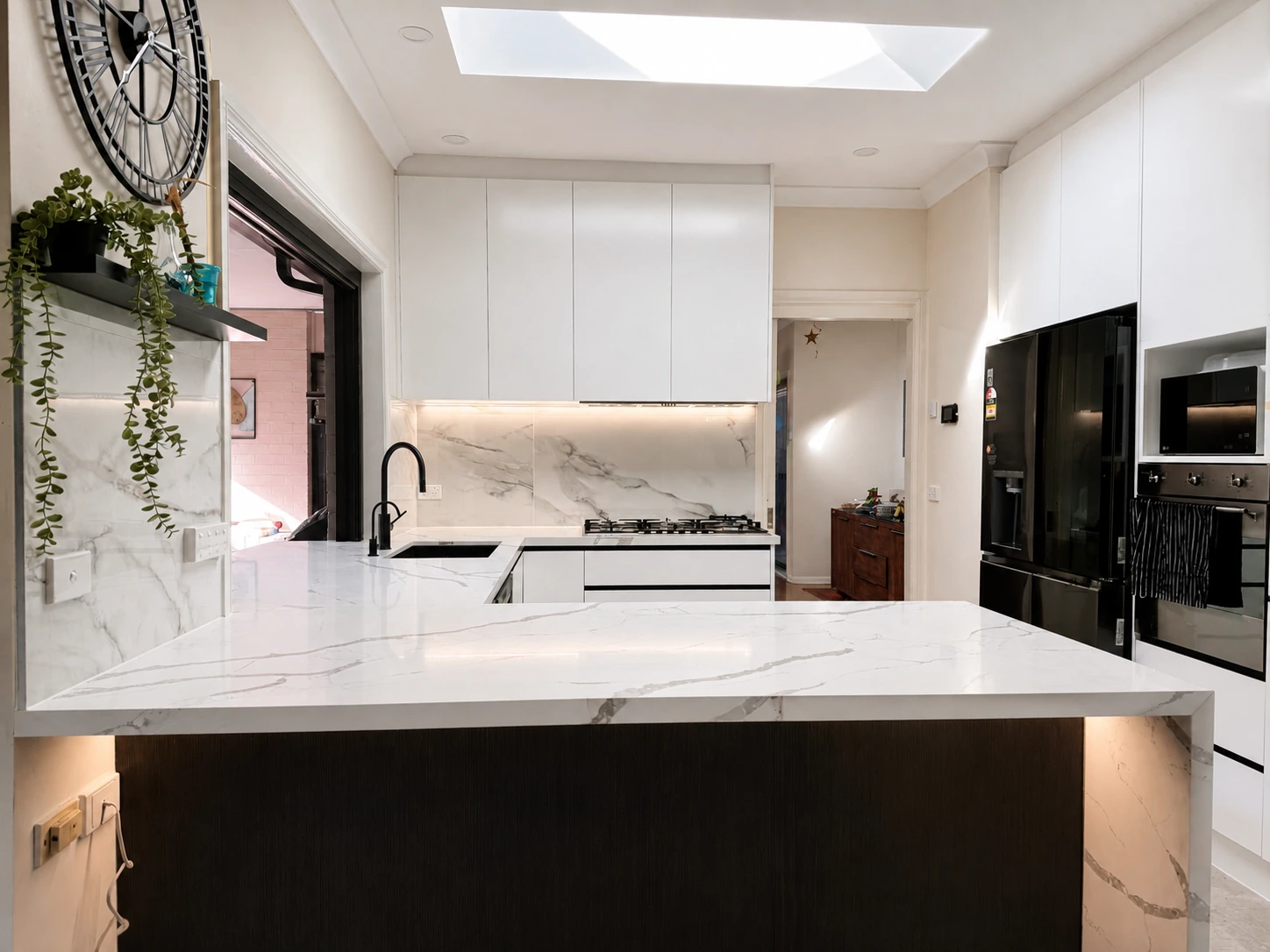 Castle Hill kitchen — marble-look waterfall island with the bi-fold servery open to a palm-filled courtyard