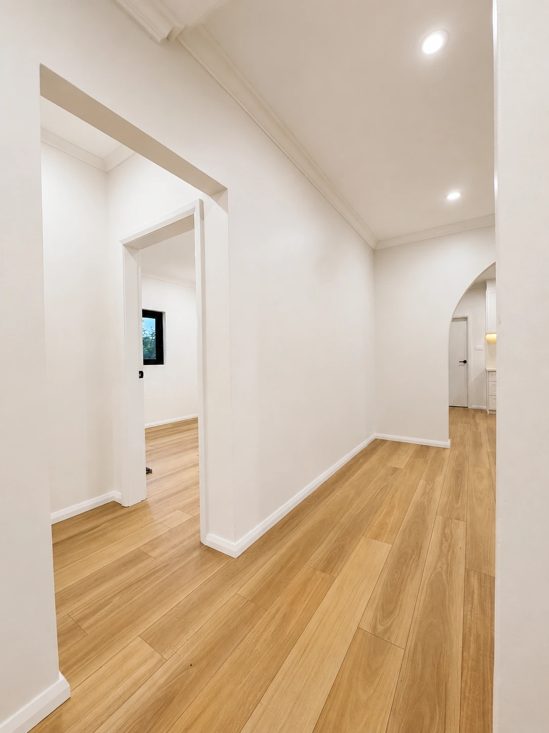 Hallway of the Strathfield home after renovation — new timber floors running through to the arched kitchen opening, with fresh cornices and repainted walls
