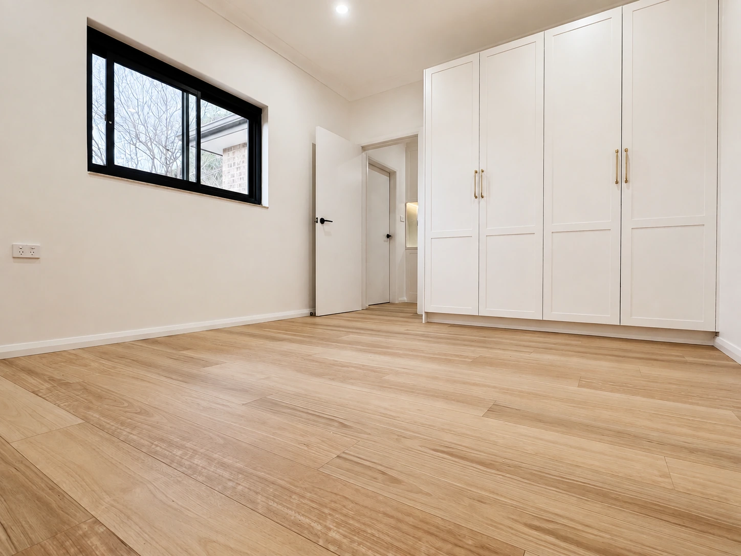 Strathfield bedroom with built-in shaker wardrobes on brass handles, a black-framed window and new timber flooring
