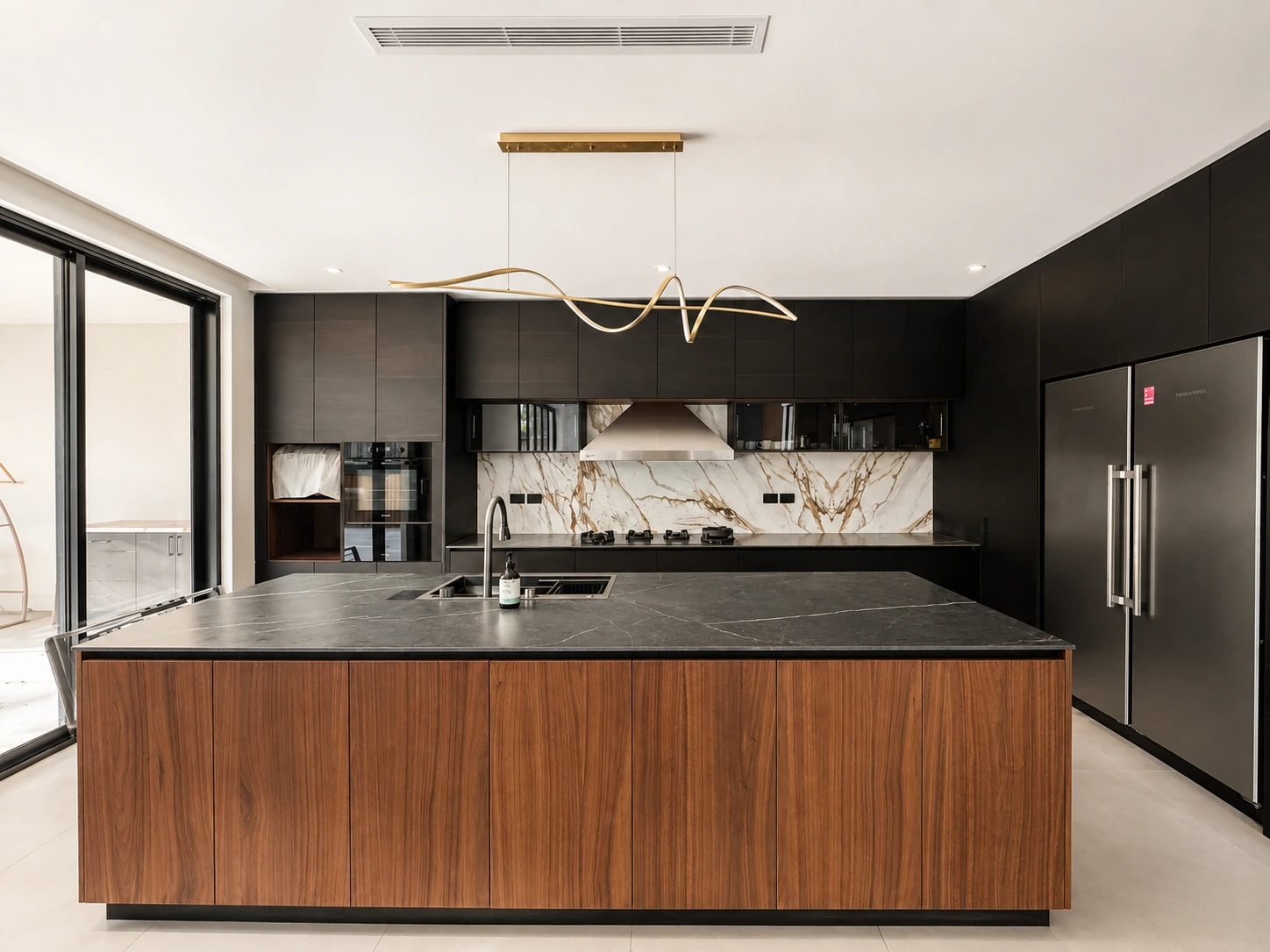 North Ryde kitchen — walnut-timber island with black stone top, a sculptural brass pendant and integrated appliances