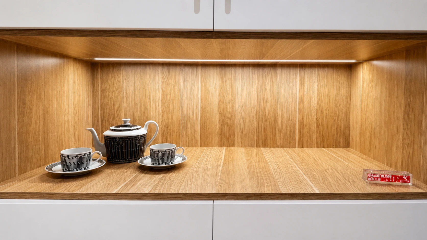 Custom oak servery niche in the Rhodes apartment joinery, an LED strip lighting the timber-lined recess between white push-to-open cabinetry