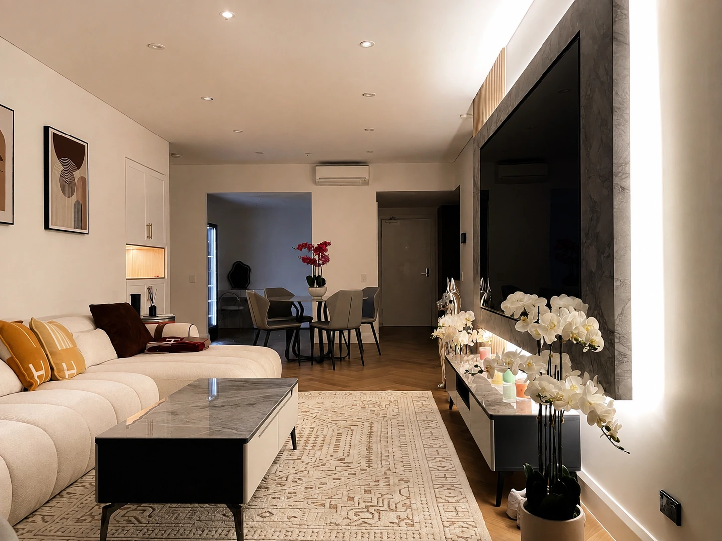 Looking from the Rhodes apartment living room through to the dining area, the lit joinery niche and herringbone oak floor carrying between the two zones